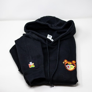 May include: Black hooded sweatshirt with a colorful puzzle piece logo on the left sleeve and a brown bear with green and red eyes on the right side.