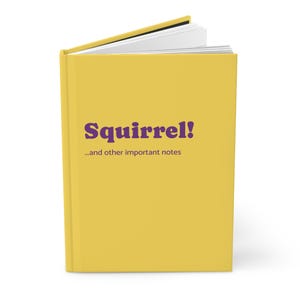 Può includere: Un libro con copertina rigida di colore giallo brillante. La copertina presenta il testo viola "Squirrel!" seguito dal testo viola più piccolo "...and other important notes". Il libro è leggermente aperto nella parte superiore, mostrando pagine bianche.