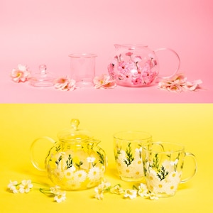May include: Two sets of teapots and cups with floral designs. The first set features a pink teapot and cup with pink flowers. The second set features a clear teapot and two cups with white flowers.