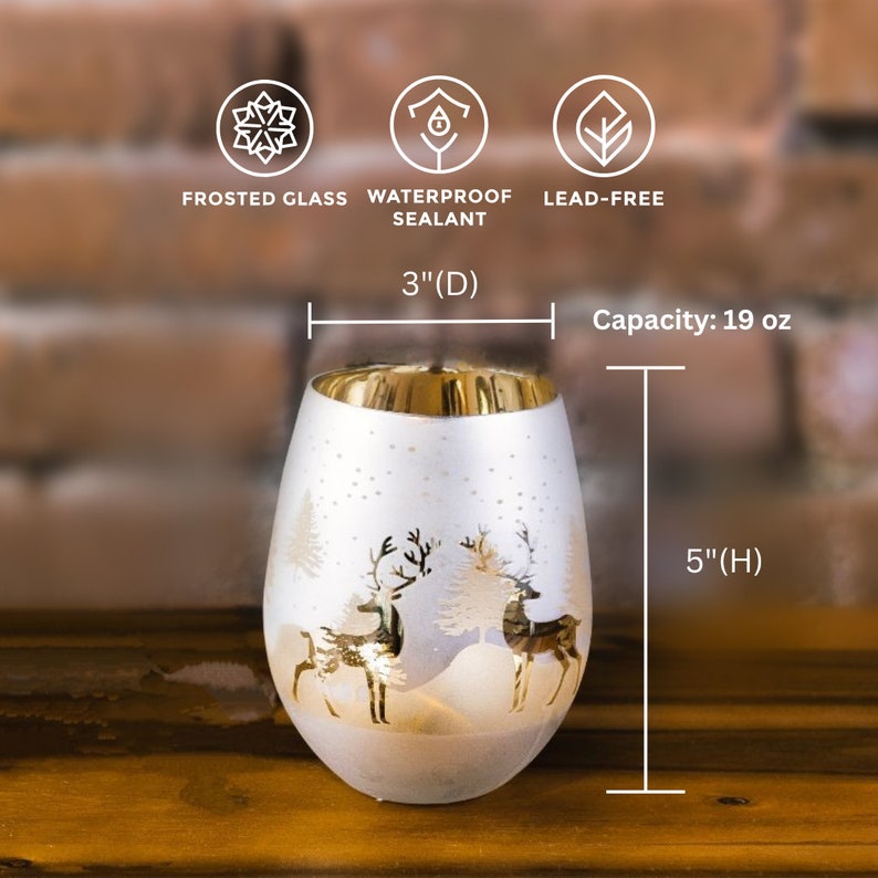 May include: White frosted glass candle holder with a gold rim and a winter scene design featuring two deer and a pine tree. The candle holder is 5 inches tall and 3 inches in diameter and has a capacity of 19 ounces.