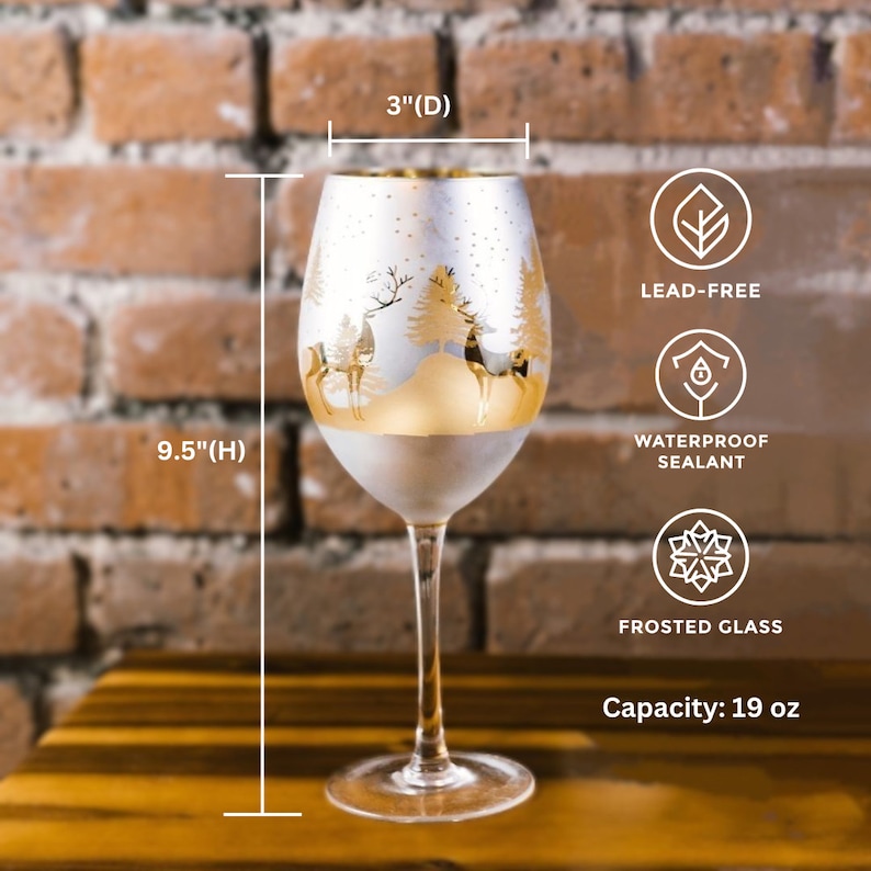 May include: A frosted glass wine glass with a gold rim and a winter scene design featuring a snowy forest and deer. The glass is 9.5 inches tall and 3 inches in diameter. It has a 19 ounce capacity and is lead-free and waterproof.
