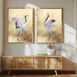 May include: Two framed art prints showcasing crane illustrations. The birds are rendered in white, black, and red against a textured gold backdrop. The artwork is displayed above a wooden cabinet, adding a touch of nature-inspired decor.