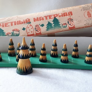 May include: A vintage wooden counting game with the Russian text "СЧЕТНЫЙ МАТЕРИАЛ" on the box. The game features 15 wooden toy trees painted in green, yellow, and black.