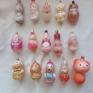 May include: A selection of vintage Christmas tree decorations. The ornaments are in the shape of various figures, including Santa Claus and animals. They are in pastel colours and have metal hangers.