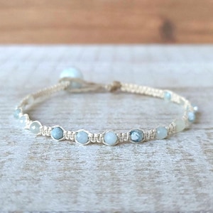 May include: A delicate bracelet made with light blue gemstone beads and a cream-colored cord.