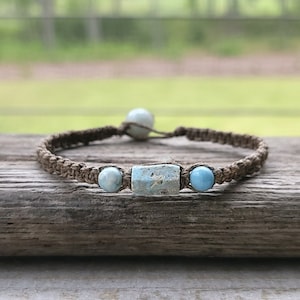 May include: A brown braided bracelet with three light blue gemstone beads, including a larger rectangular bead in the centre.