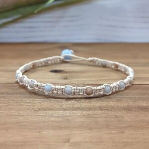 May include: A light blue and beige beaded bracelet with a macrame knot design. The bracelet is made with natural materials and has a simple, elegant style.