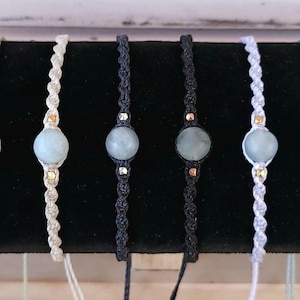 May include: Seven bracelets with different colored cords and a light blue gemstone bead in the center of each bracelet.