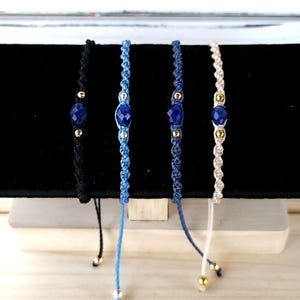 May include: Four adjustable bracelets with blue gemstone beads and gold accents. The bracelets are made with black, blue, and cream colored cords.