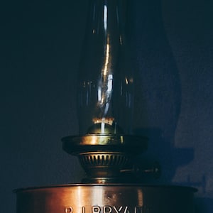 May include: A vintage copper oil lamp with a glass chimney and a brass base. The lamp has a label that reads "P.J. BRYAN BRISTOL".