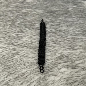 Puede incluir: Un brazalete negro de cuentas con un dise&ntilde;o geom&eacute;trico. El brazalete est&aacute; hecho de peque&ntilde;as cuentas redondas que est&aacute;n enhebradas juntas en un patr&oacute;n que se asemeja a una serie de hex&aacute;gonos conectados.