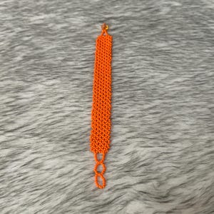 Puede incluir: Un brazalete de cuentas de color naranja brillante con un cierre simple.
