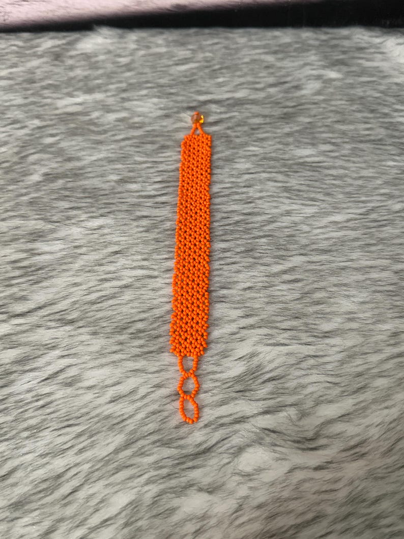 Puede incluir: Un brazalete de cuentas de color naranja brillante con un cierre simple.