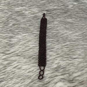 Puede incluir: Un brazalete de cuentas de color morado oscuro con un cierre simple.