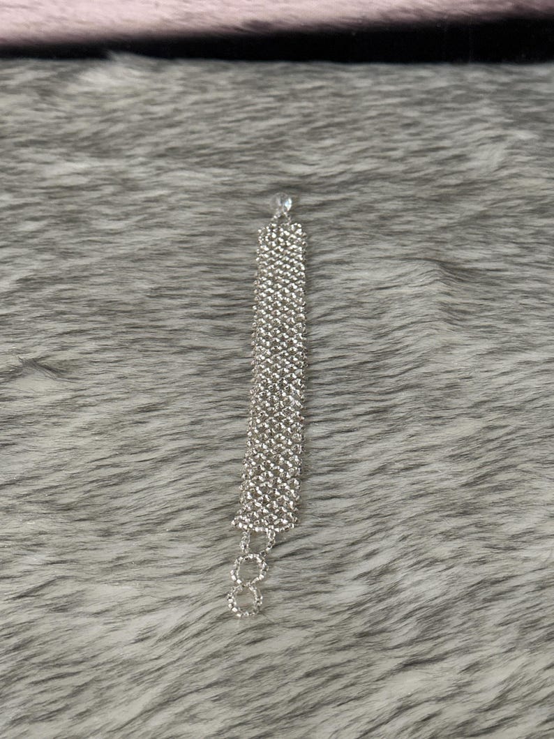 Puede incluir: Un brazalete plateado con un dise&ntilde;o de cadena hecho de peque&ntilde;os diamantes de imitaci&oacute;n transparentes.