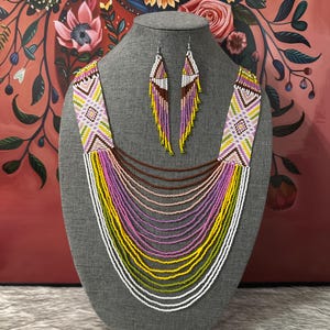 Op de afbeelding: Een meerrijige kralenketting met een geometrisch patroon in wit, roze, geel en groen. De ketting wordt geleverd met bijpassende oorbellen.