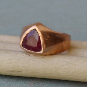 May include: A copper ring with a triangular red gemstone set in the center.