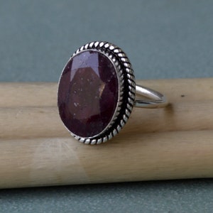 Puede incluir: Un anillo de plata con una gran piedra preciosa ovalada de color púrpura oscuro engastada en una banda de plata retorcida.