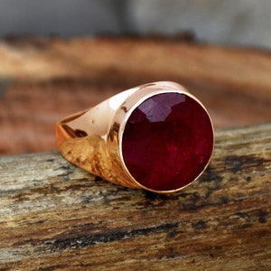 May include: A gold ring with a large, round, red ruby gemstone.