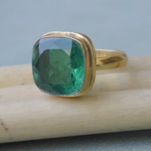 May include: A gold ring featuring a large, square-shaped, emerald green gemstone.