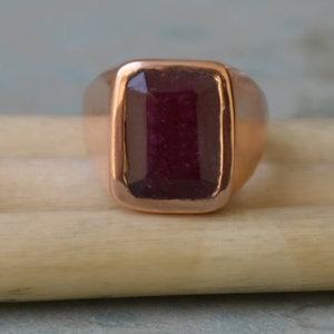May include: A rose gold ring with a large, rectangular, dark red gemstone.