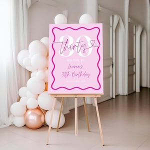 May include: Pink birthday sign with a white border and white text that says "Thirty" with a heart and "Celebrating the Lauren's 30th Birthday".
