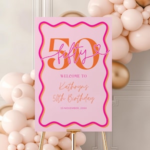 May include: Pink and orange welcome sign with a wavy border. The sign says "Welcome to Kathryn's 50th Birthday" and features a large orange number 50 with the word "fifty" in pink script. The sign is propped up on a gold easel.