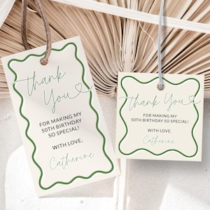 May include: Two gift tags with a cream background and a green wavy border. The tags read "Thank You" and "For making my 50th birthday so special!" with the name "Catherine" at the bottom. The tags are hanging by a string.