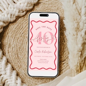 May include: A smartphone displays a pink digital invitation for a 40th birthday. The invitation reads "Save the Date" and "forty" in a script font, with the name "Carla Robertson" and event details. The phone rests on a beige textured surface.