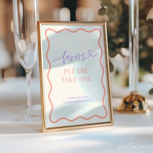Könnte beinhalten: Ein goldgerahmtes Schild mit dem Wort "favors" in lila Schrift und dem Text "PLEASE TAKE ONE" in Rosa. Das Schild hat einen wellenförmigen rosa Rand und den Text "THANK YOU FOR CELEBRATING WITH US!" unten.