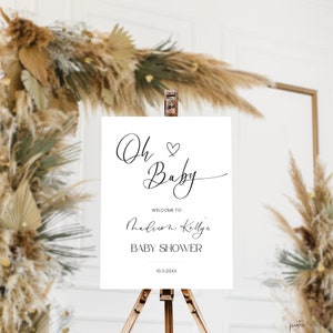 Op de afbeelding: Een wit bord met zwarte kalligrafie waarop "Oh Baby" staat met een hartje. Onder de tekst staat "Welkom op de babyshower van Madison Kelly" en de datum "10.11.20XX".