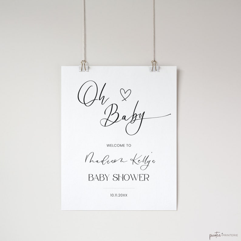 Op de afbeelding: Een wit bord met zwarte tekst die "Oh Baby" zegt met een hartje. Het bord zegt ook "Welkom bij de babyshower van Madison Kelly" en de datum "10.11.20XX".