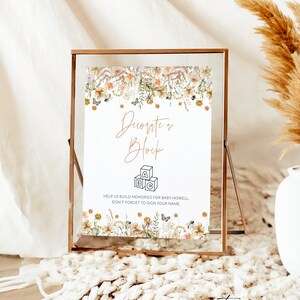 May include: A sign with a floral border and the text "Decorate a Block" with a drawing of three blocks that spell "ABC". The sign also includes the text "Help us build memories for baby Howell. Don't forget to sign your name."