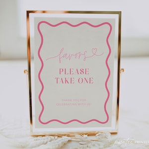 May include: A framed sign with gold trim and a white background. The sign has pink text that reads "favors, PLEASE TAKE ONE, THANK YOU FOR CELEBRATING WITH US!" The sign has a pink wavy border.
