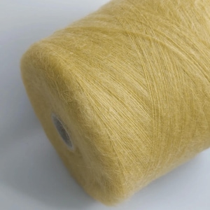 May include: A spool of soft, yellow yarn. The yarn is tightly wound, with visible strands and a slightly fuzzy texture. The color is a muted, warm yellow, suitable for knitting or crocheting projects. The spool has a cardboard core.