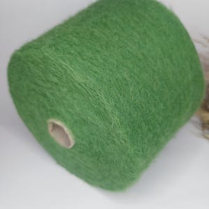 May include: A large spool of green yarn, ideal for knitting or crocheting projects. The yarn has a soft, fuzzy texture and a vibrant, solid color. The spool is cylindrical with a cardboard core, perfect for crafting.