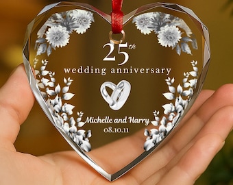Könnte beinhalten: Ein klarer, herzförmiger Anhänger mit rotem Band. Er trägt die Aufschrift "25. Hochzeitstag", zwei ineinander verschlungene Ringe und die Namen "Michelle und Harry" mit einem Datum. Weiße Blumendesigns umranden den Text.