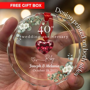 Puede incluir: Adorno redondo de cristal transparente con borde dorado, con el texto "40 aniversario de bodas" y "Ruby". El adorno tiene una gema roja en forma de corazón y detalles florales. También se ve el texto "Joseph & Melania, 19 de octubre de 2025". También se ve el texto "Diseño impreso en ambas caras".