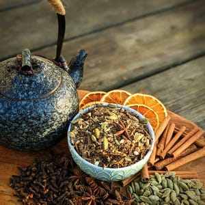 May include: A blue teapot with a brown handle and a bowl of loose leaf tea blend with dried orange slices, cinnamon sticks, cloves, star anise, and cardamom pods.