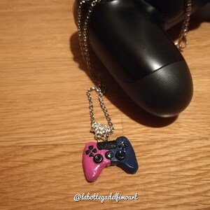Può includere: Una collana con catena argentata con un ciondolo a forma di controller per videogiochi rosa e blu. Il ciondolo è realizzato in pasta polimerica e presenta un pulsante PlayStation nero.