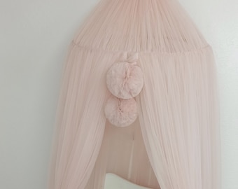 May include: A powder pink tulle canopy with pom poms hangs over a white crib with a white and pink braided pillow. The text "Powder Pink" is visible in the bottom right corner of the image.