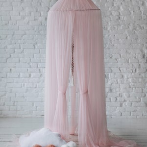 May include: A pink tulle canopy with a white cloud-shaped pillow and brown pom-poms on a white wooden floor.
