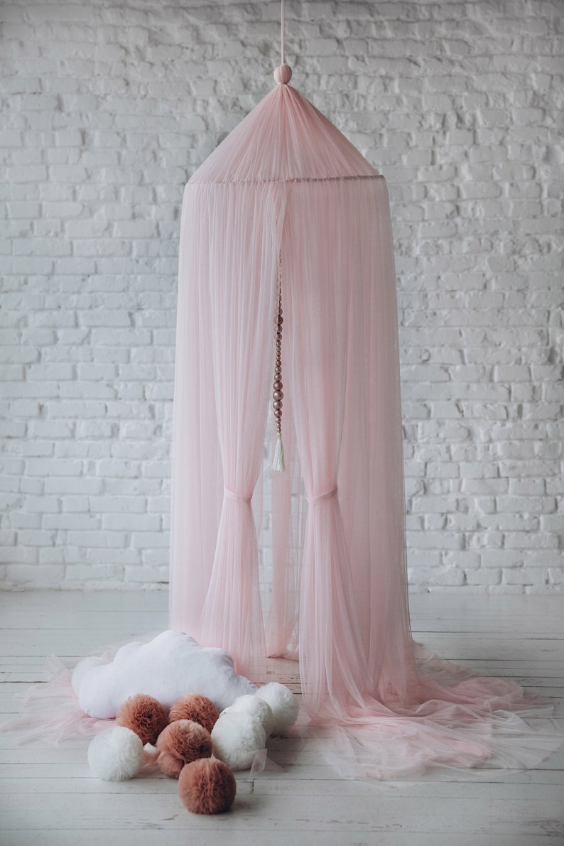 May include: A pink tulle canopy with a white cloud-shaped pillow and brown pom-poms on a white wooden floor.