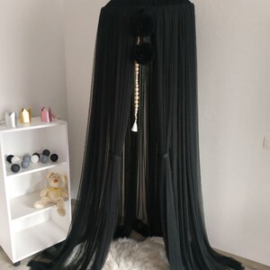 May include: Black sheer canopy with a white beaded tassel hanging from the top. The canopy is made of a soft, flowing fabric and has a delicate, ethereal look.