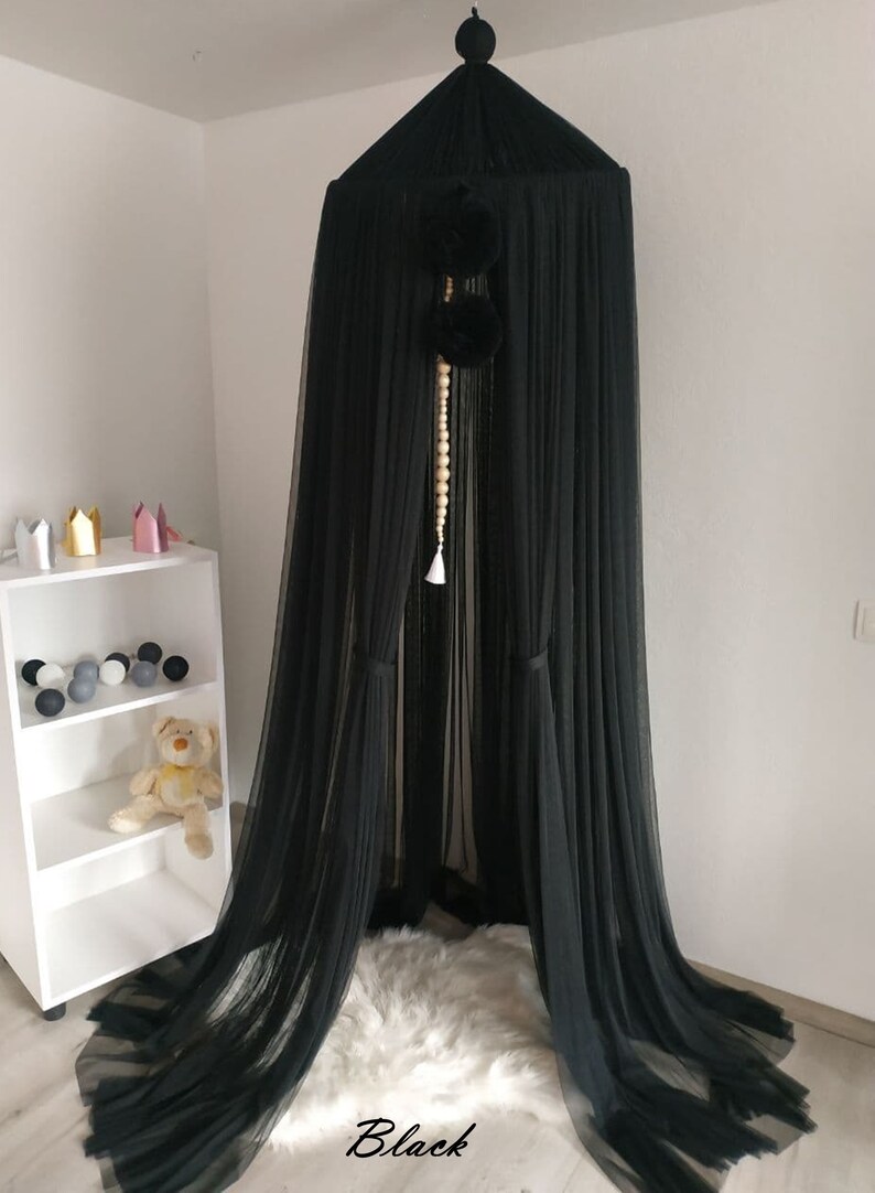 May include: Black sheer canopy with a white beaded tassel hanging from the top. The canopy is made of a soft, flowing fabric and has a delicate, ethereal look.
