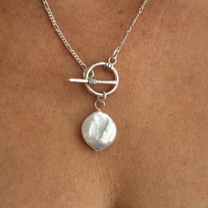 Puede incluir: Un collar de cadena de plata con un cierre de palanca y un gran colgante de perla blanca.