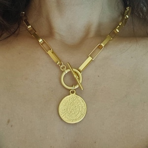 May include: A gold chain necklace with a large, round pendant featuring intricate details. The pendant is attached to the chain with a toggle clasp.