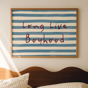 May include: A bedroom scene featuring a wooden bed frame and bedding with a striped pattern. Above the bed hangs a framed artwork with blue and white stripes and the text "Long Live Boyhood" in red.