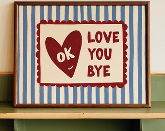 May include: A framed artwork with a brown border, featuring a red heart with "ok" inside, and the words "LOVE YOU BYE" on a cream background. The background has blue and white vertical stripes. The artwork is displayed on a green shelf.