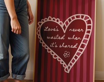 Può includere: Una stampa artistica incorniciata con uno sfondo a righe rosse e rosa. Un cuore bianco con la scritta "Love's never wasted when it's shared" è centrato sulla stampa. La cornice è di colore marrone chiaro.